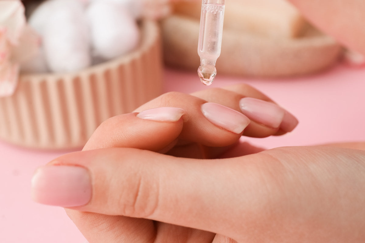 A woman applying oil to her cuticles on a pink background