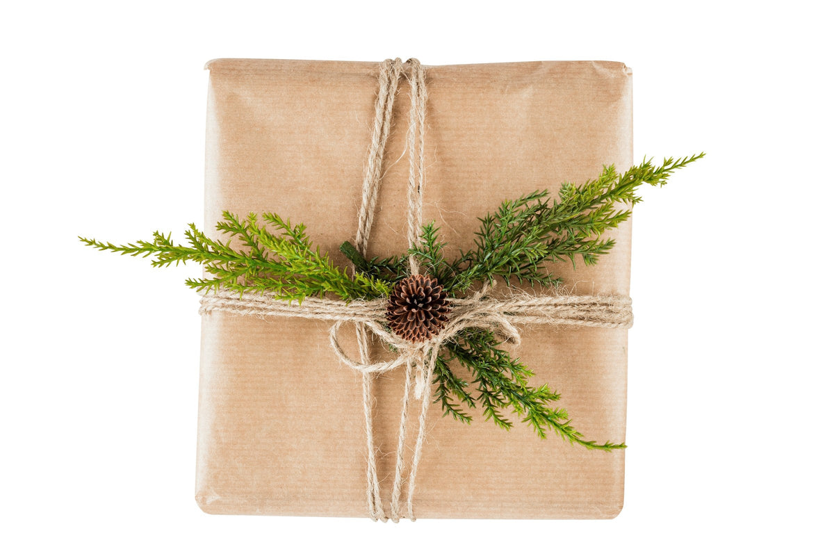 A small gift wrapped in kraft paper and twine with green sprigs and a pine cone